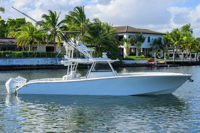 Slide: The Image of 2021 Yellowfin 42 boat on a calm waterway with palm trees and houses in the background. - 2