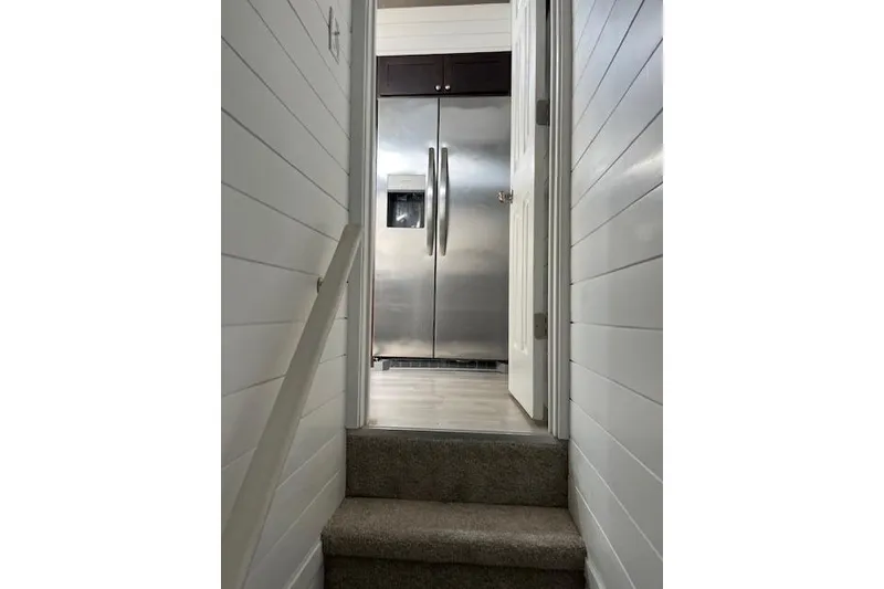 Slide: The Image of Staircase leading to a modern kitchen with stainless steel refrigerator in a 2021 Harbor Cottage. - 11