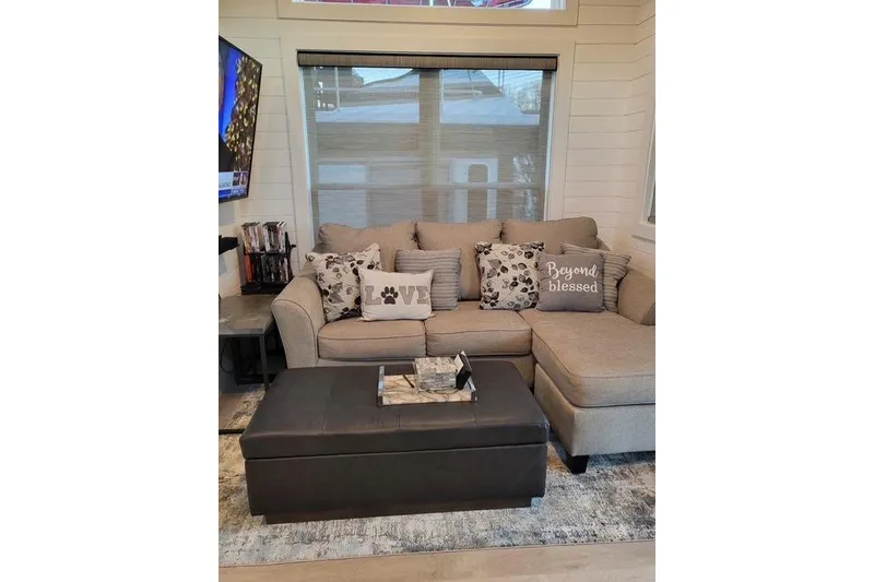 Slide: The Image of Cozy living room with sectional sofa, decorative pillows, and ottoman in a Harbor Cottage model. - 4