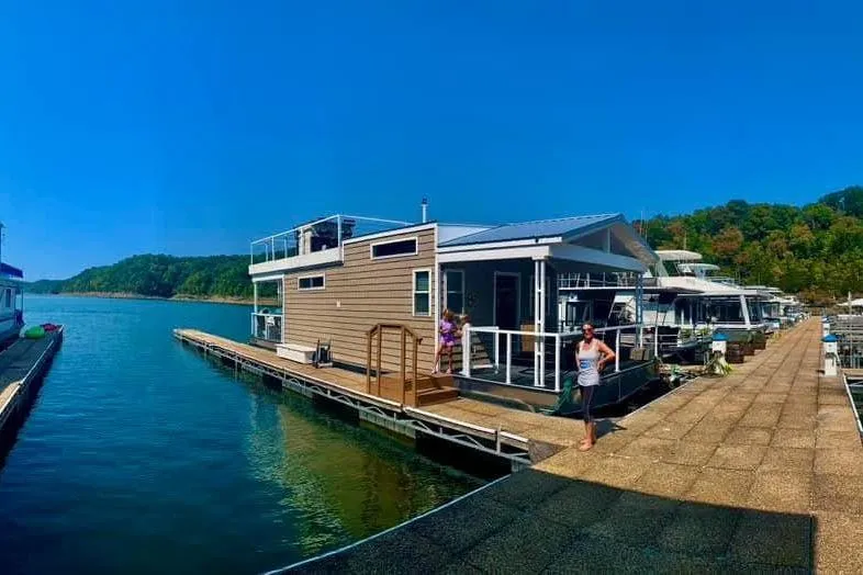 Slide: The Image of Modern 2021 Harbor Cottage houseboat docked on a serene lake with clear blue skies. - 40