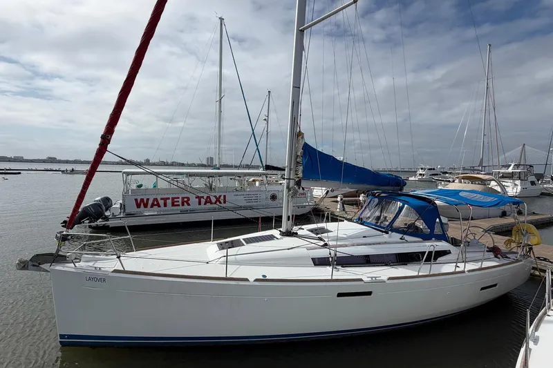 The Image of 2018 Jeanneau Sun Odyssey 389 sailboat docked near water taxi, under cloudy sky. - 2