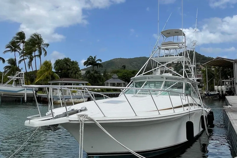 Slide: The Image of 1998 Cabo 45 Express yacht docked, surrounded by palm trees and mountains. - 2