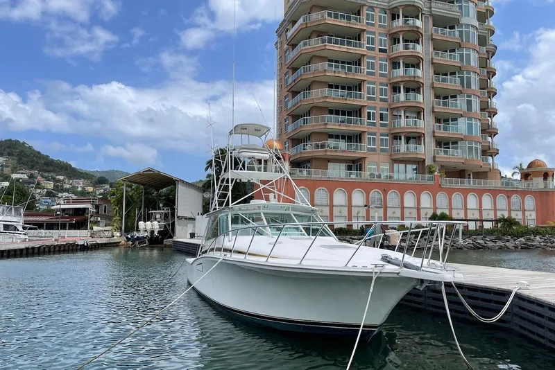 Slide: The Image of 1998 Cabo 45 Express yacht docked near a waterfront building under a blue sky. - 3