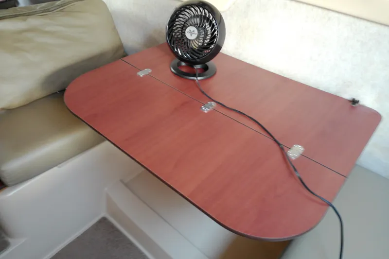 Slide: The Image of Wooden table with a small fan inside a 2011 MacGregor 26M boat interior. - 21