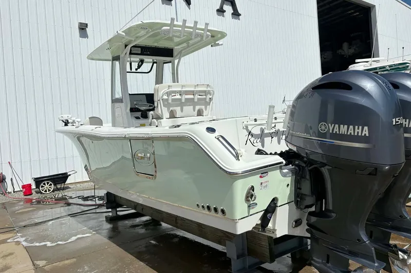 The Image of 2021 Sea Hunt boat with dual Yamaha 150 engines, parked near a white building. - 0