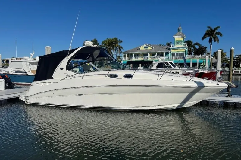 The Image of 2005 Sea Ray Sundancer 320 docked at marina, clear blue sky, waterfront building in background. - 1