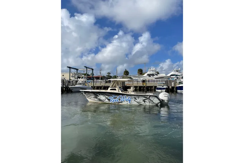 The Image of 2023 Grady-White Canyon 306 boat docked, featuring "Reel Wolf" design, under a partly cloudy sky. - 0