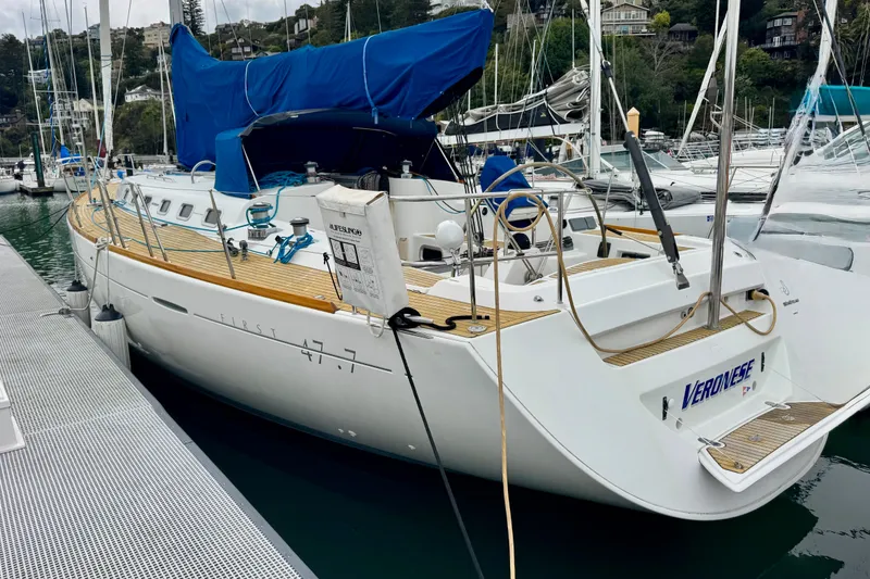 Slide: The Image of 2003 Beneteau First 47.7 sailboat docked at marina, featuring sleek design and blue cover. - 2