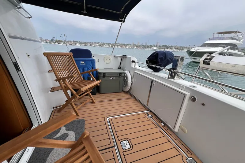Slide: The Image of 2003 Carver 444 Cockpit Motor Yacht with wooden deck chairs and scenic harbor view. - 35