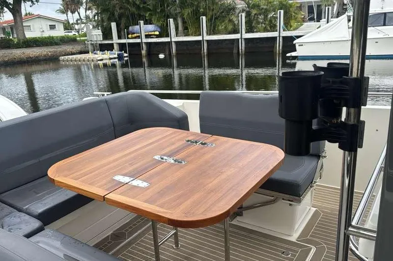 Slide: The Image of Nimbus T11 2021 boat interior with wooden table and gray seating by the water. - 12
