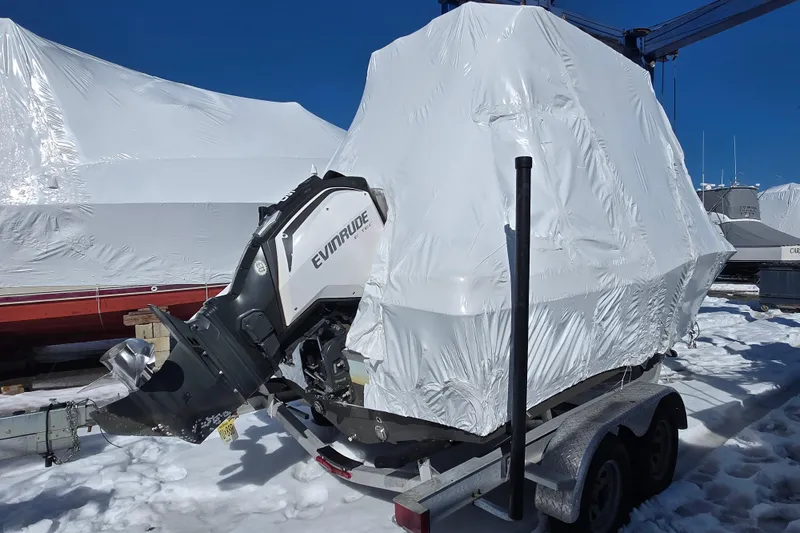 Slide: The Image of 2018 Clearwater 2000 Center Console boat covered in white tarp, on a snowy trailer. - 7