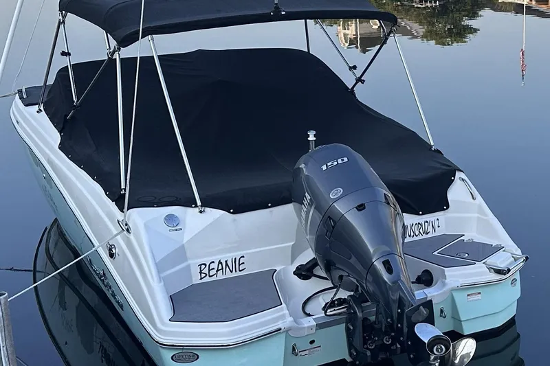 Slide: The Image of 2023 NauticStar 223 DC boat with black cover and 150 HP engine on calm water. - 2