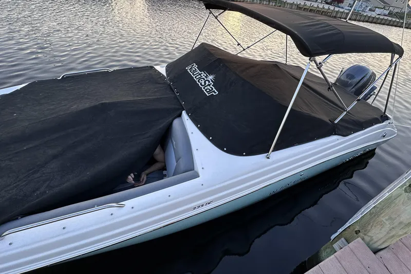 Slide: The Image of 2023 NauticStar 223 DC boat with black cover docked on calm water. - 4