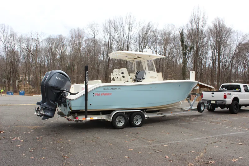 Slide: The Image of 2022 Cobia 280 Center Console boat on trailer, parked in wooded area. - 2
