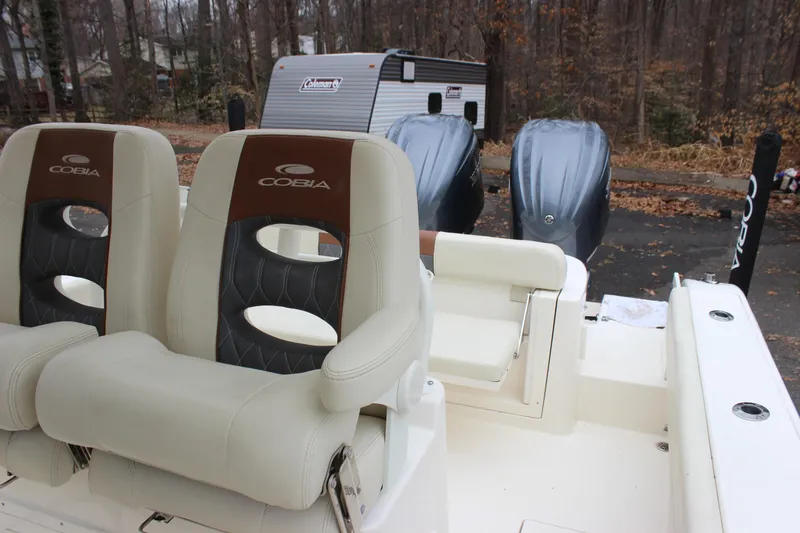 Slide: The Image of 2022 Cobia 280 Center Console boat seats with dual outboard motors in wooded area. - 22