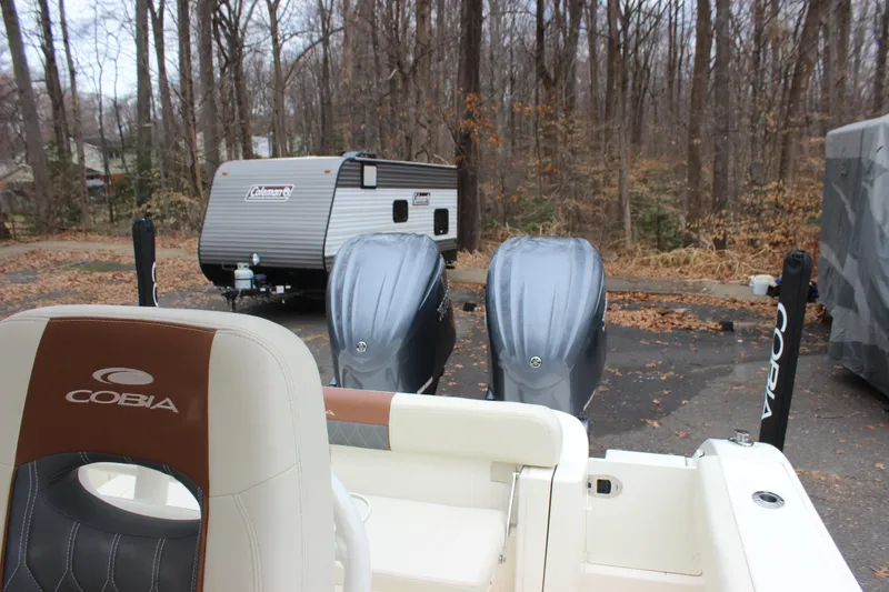 Slide: The Image of 2022 Cobia 280 Center Console boat with dual engines, parked near a forested area. - 23