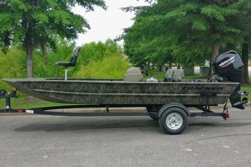 The Image of 2026 Tracker Grizzly 1754 SC boat on trailer, parked outdoors with trees in background. - 0