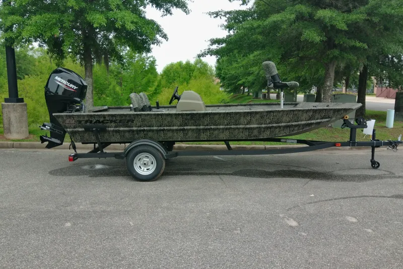 Slide: The Image of 2026 Tracker Grizzly 1754 SC boat on trailer, parked outdoors with trees in background. - 2