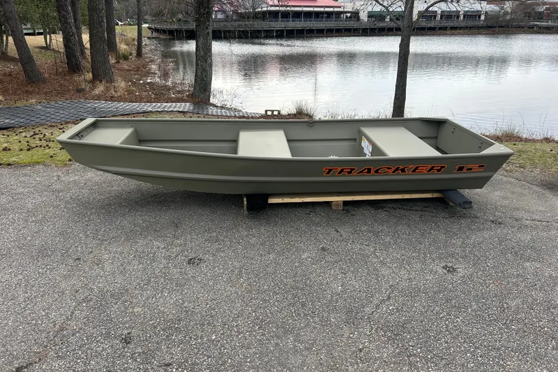 The Image of 2026 Tracker Grizzly 12 Jon boat on lakeside pavement, surrounded by trees. - 0