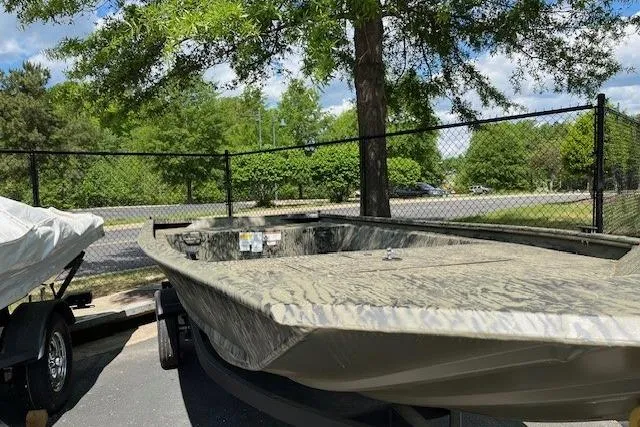Slide: The Image of 2026 Tracker Grizzly 1648 Utility boat in a parking lot, surrounded by trees and fencing. - 2