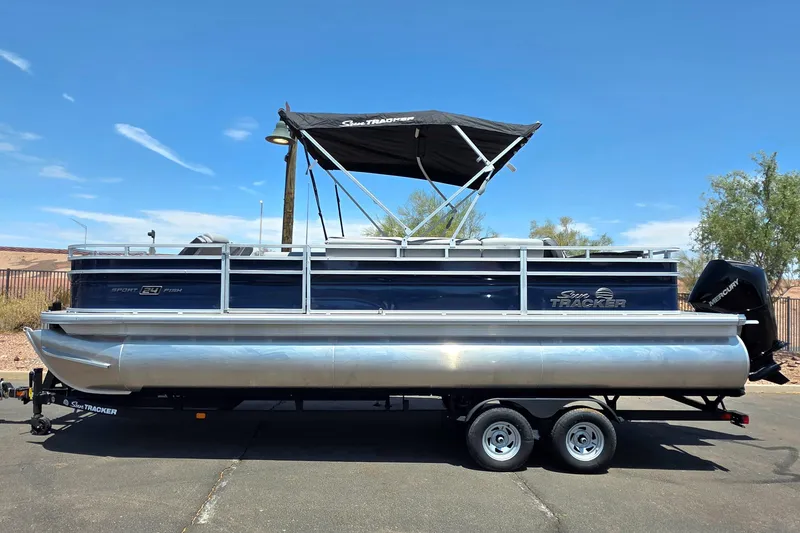 Slide: The Image of 2026 Sun Tracker Sportfish 24 XP3 pontoon boat on trailer, under clear blue sky. - 1
