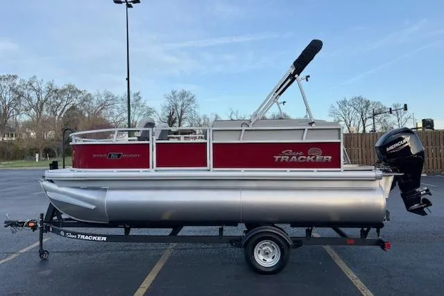 Slide: The Image of 2026 Sun Tracker Bass Buggy 16 XL Select pontoon boat on trailer in parking lot. - 100
