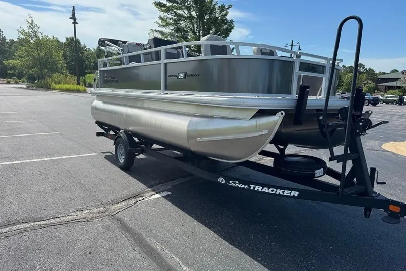 Slide: The Image of 2026 Sun Tracker Bass Buggy 16 XL Select pontoon boat on trailer in parking lot. - 2