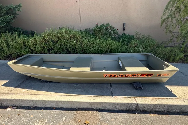 Slide: The Image of 2026 Tracker Grizzly 12 Jon boat on pavement, surrounded by greenery. - 1