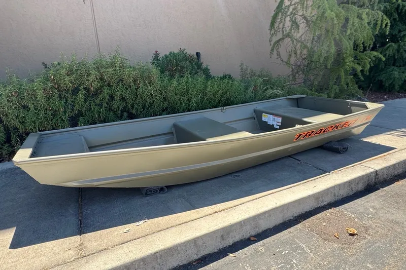 Slide: The Image of 2026 Tracker Grizzly 12 Jon boat on pavement, surrounded by greenery. - 2