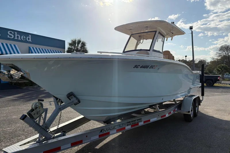Slide: The Image of 2023 Scout 277 LXF boat on trailer, parked outside a building under a sunny sky. - 6