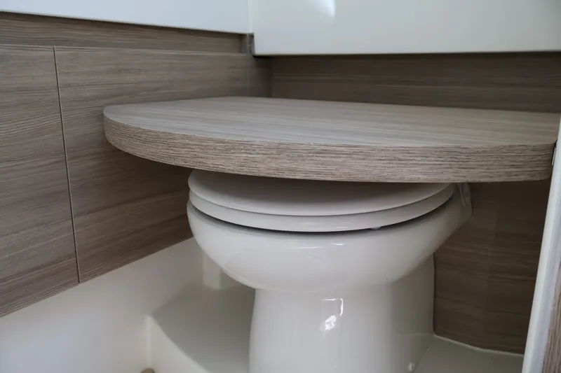 Slide: The Image of A modern boat bathroom with a toilet and a foldable wooden table. - 42