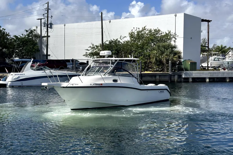 Slide: The Image of 2006 Boston Whaler 285 Conquest boat on water near marina, clear sky background. - 7