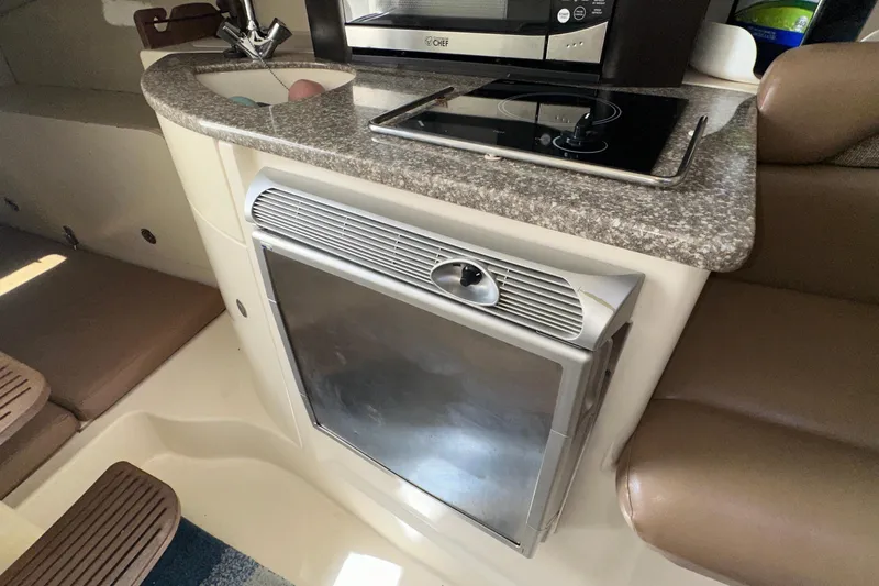 Slide: The Image of 2006 Boston Whaler 285 Conquest interior with kitchenette, featuring stove, sink, and seating area. - 78