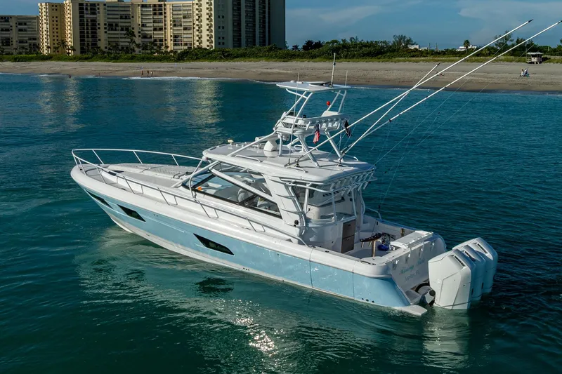 Slide: The Image of 2023 Intrepid 477 Evolution boat cruising near a beach with buildings in the background. - 5