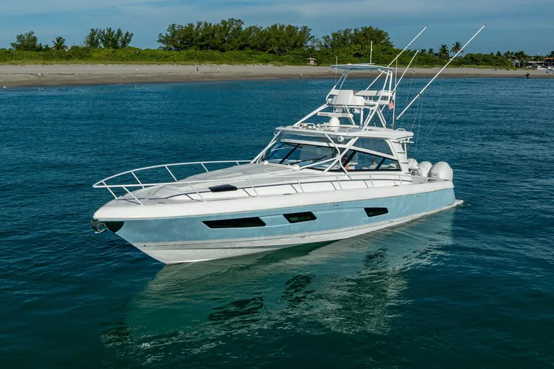 Slide: The Image of 2023 Intrepid 477 Evolution yacht cruising on calm blue waters near a sandy shoreline. - 7