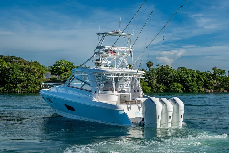 Slide: The Image of 2023 Intrepid 477 Evolution boat cruising on a sunny day with lush greenery backdrop. - 77