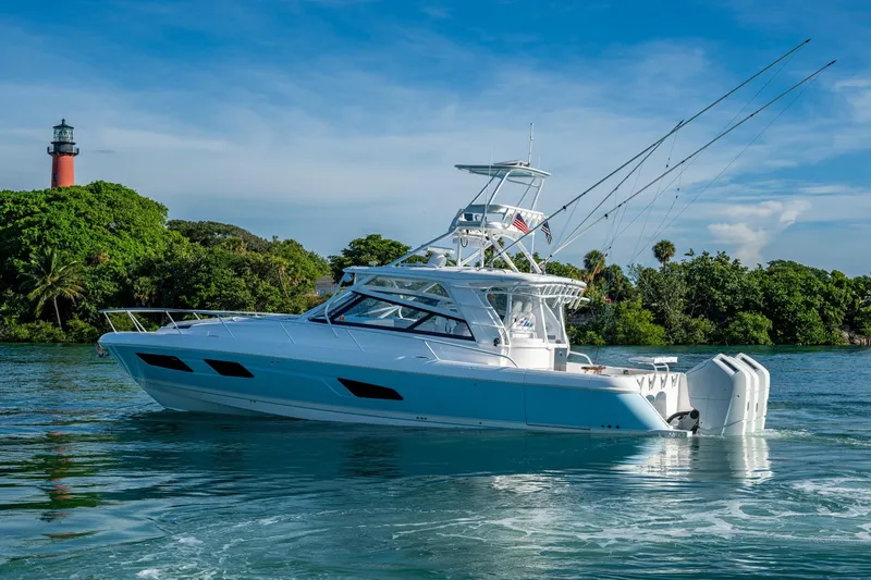 Slide: The Image of 2023 Intrepid 477 Evolution yacht cruising near a lighthouse and lush greenery. - 79