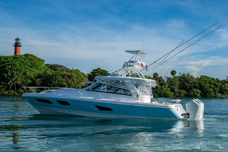 Slide: The Image of 2023 Intrepid 477 Evolution yacht cruising near lush greenery and lighthouse. - 80