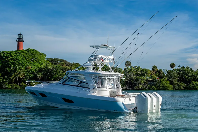 Slide: The Image of 2023 Intrepid 477 Evolution yacht near a lighthouse and lush greenery. - 83