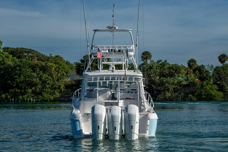 Slide: The Image of 2023 Intrepid 477 Evolution boat on water, rear view with lush greenery background. - 84