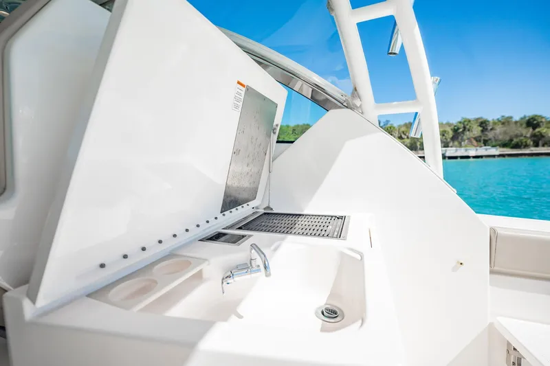Slide: The Image of 2017 Pursuit DC 325 Dual Console boat interior with sink and grill, near turquoise water. - 40
