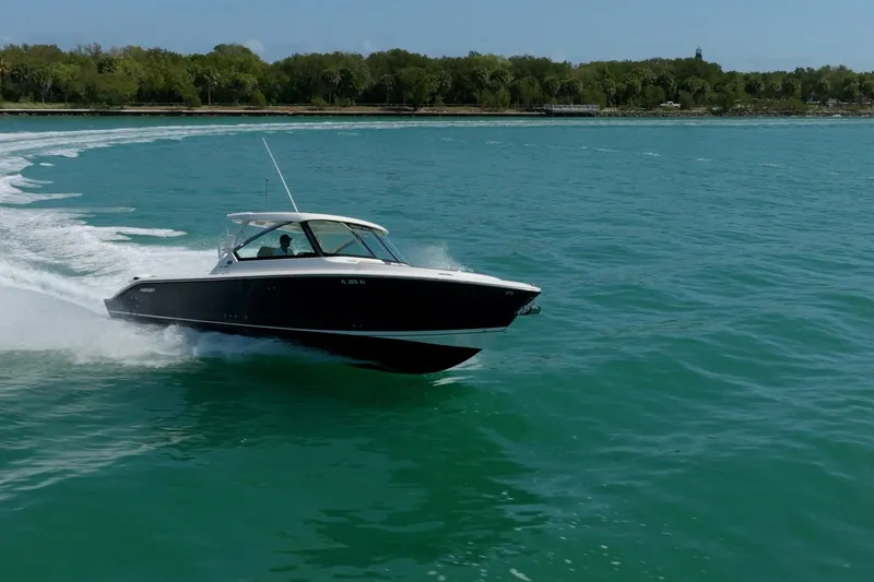 Slide: The Image of 2017 Pursuit DC 325 Dual Console boat cruising on turquoise water near a forested shoreline. - 67
