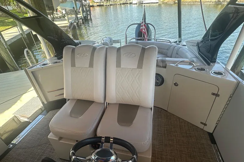 Slide: The Image of 2017 Harris V270 boat interior with plush seating and steering wheel, docked by the water. - 11