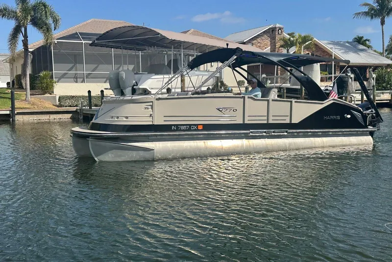 Slide: The Image of 2017 Harris V270 pontoon boat cruising on a sunny day near waterfront homes. - 2