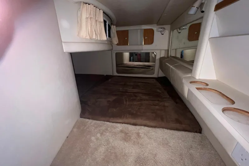 Slide: The Image of 1999 Sea Ray 290 Sundancer cabin interior with bed, storage, and window curtains. - 31