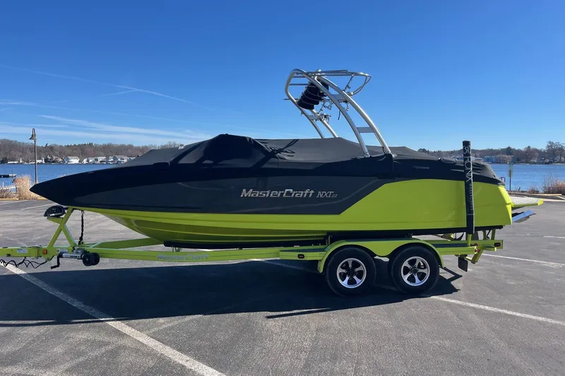 Slide: The Image of 2017 MasterCraft NXT22 boat on trailer, covered, near a lake under clear blue sky. - 4