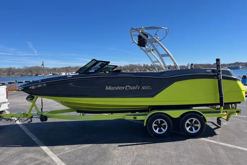 Slide: The Image of 2017 MasterCraft NXT22 boat on trailer, vibrant green and black design, parked near a lake. - 6