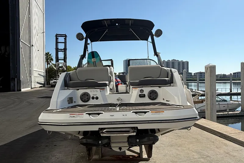 Slide: The Image of 2021 Scarab 255 ID boat docked, rear view with seating and speakers, sunny marina backdrop. - 6