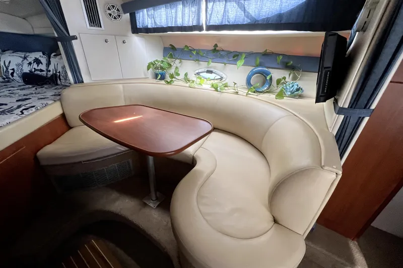 Slide: The Image of 2007 Bayliner 305 interior with curved seating, wooden table, and decorative plants. - 13