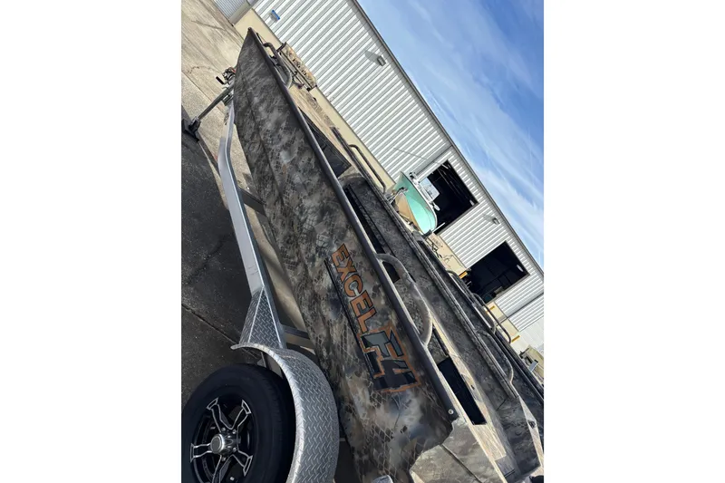 Slide: The Image of 2023 Excel 1754 Shallow Water F4 boat with camouflage design, parked outside a warehouse. - 15